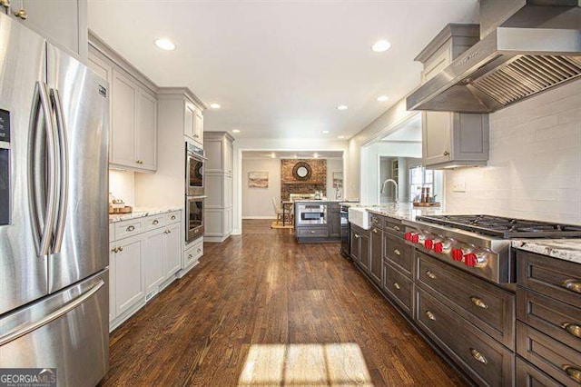 kitchen featuring light stone counters, appliances with stainless steel finishes, wall chimney range hood, and dark wood-style flooring