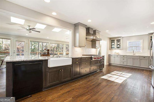 kitchen with a sink, dishwasher, dark wood finished floors, and wall chimney range hood