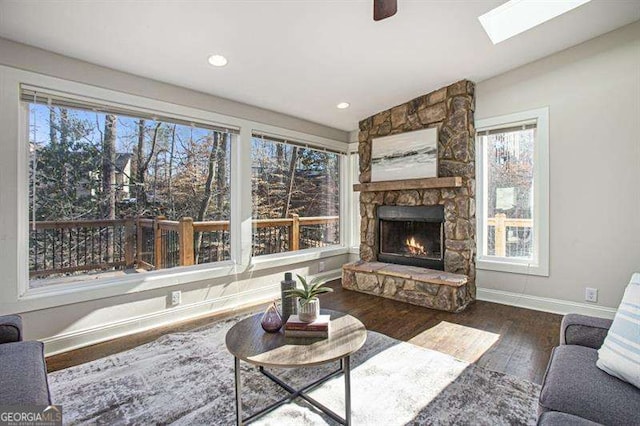 living room featuring wood finished floors, recessed lighting, a skylight, a fireplace, and baseboards