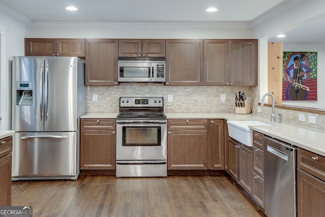 kitchen featuring a sink, light countertops, ornamental molding, appliances with stainless steel finishes, and dark wood-style flooring