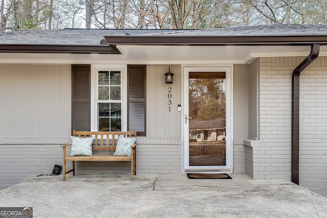 property entrance with brick siding, covered porch, and roof with shingles