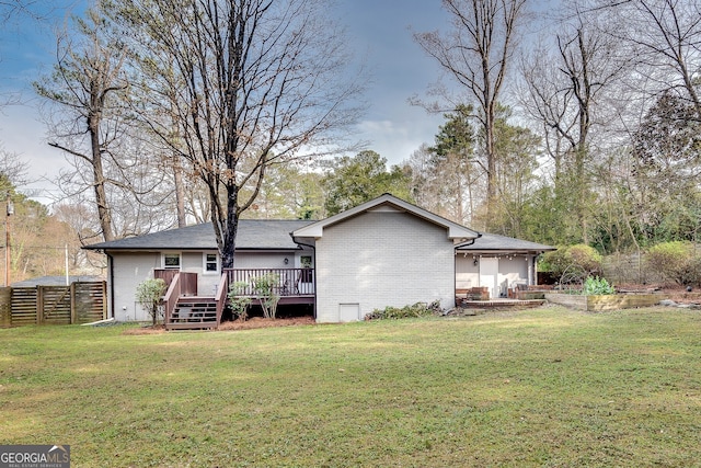 rear view of property with a wooden deck, brick siding, a lawn, and fence