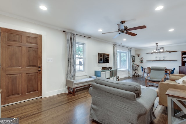 living room featuring wood finished floors, baseboards, recessed lighting, crown molding, and ceiling fan with notable chandelier