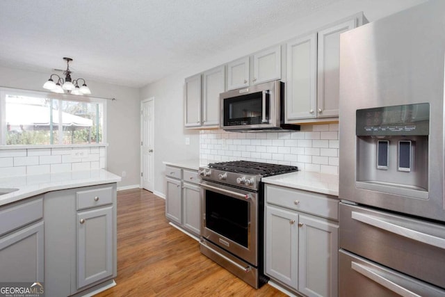 kitchen with an inviting chandelier, light wood-style floors, gray cabinets, and appliances with stainless steel finishes