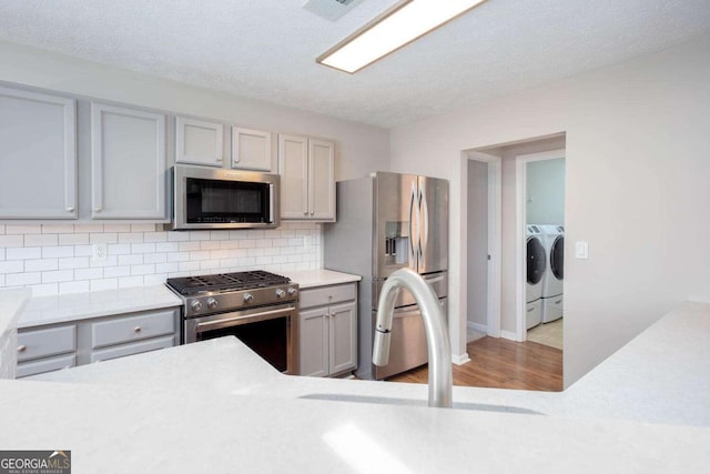 kitchen featuring gray cabinetry, washer and clothes dryer, backsplash, appliances with stainless steel finishes, and light countertops