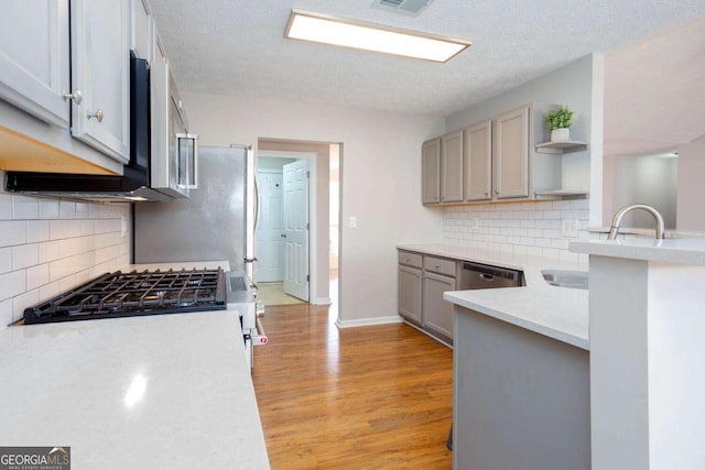 kitchen featuring light wood finished floors, gray cabinetry, open shelves, appliances with stainless steel finishes, and light countertops