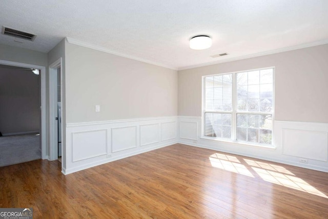 spare room with a wainscoted wall, wood finished floors, visible vents, and ornamental molding