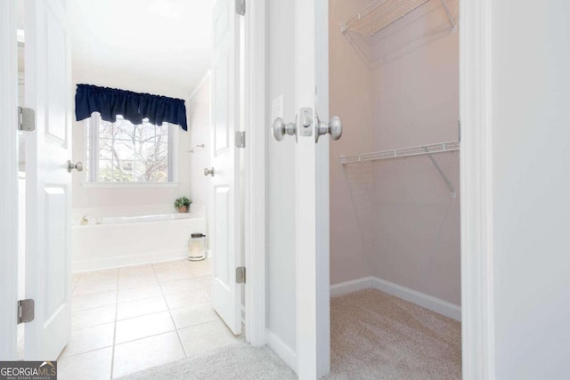 full bathroom with a walk in closet, tile patterned floors, a garden tub, and baseboards