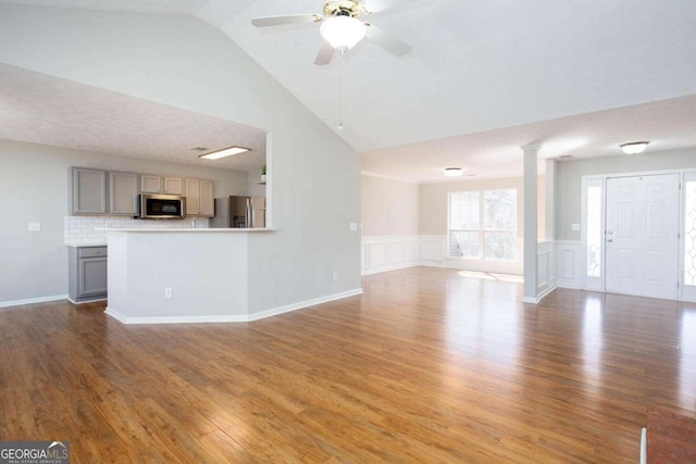 unfurnished living room featuring ornate columns, wainscoting, a ceiling fan, and wood finished floors