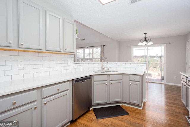 kitchen with a peninsula, an inviting chandelier, a sink, stainless steel dishwasher, and backsplash