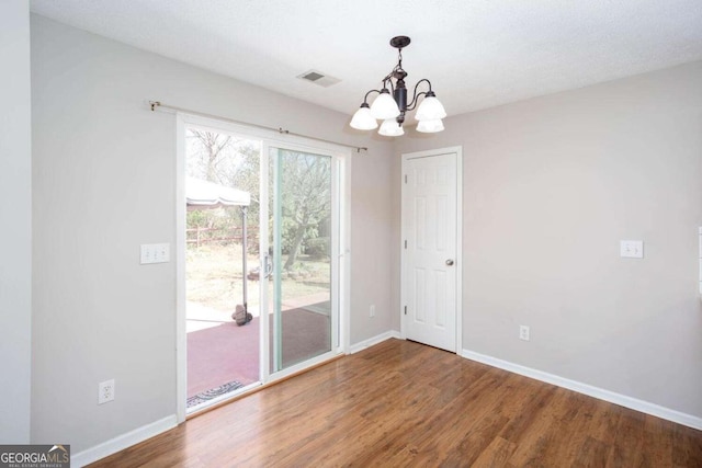 spare room with visible vents, wood finished floors, baseboards, and a chandelier