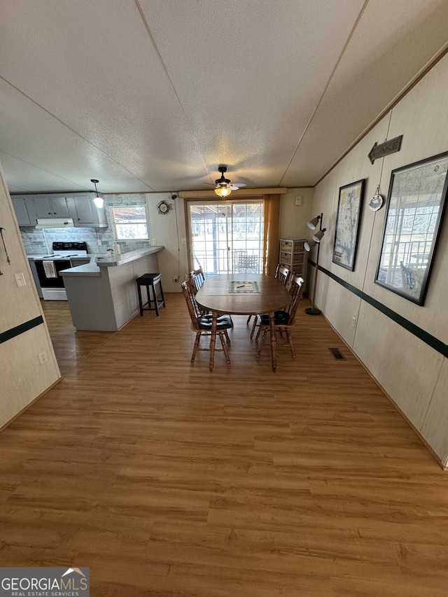 dining area featuring visible vents, a ceiling fan, a textured ceiling, light wood finished floors, and lofted ceiling