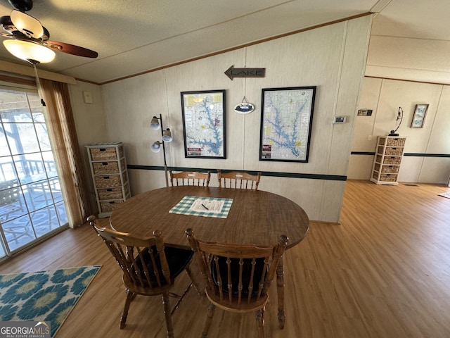 dining area with a ceiling fan, wood finished floors, ornamental molding, vaulted ceiling, and a textured ceiling