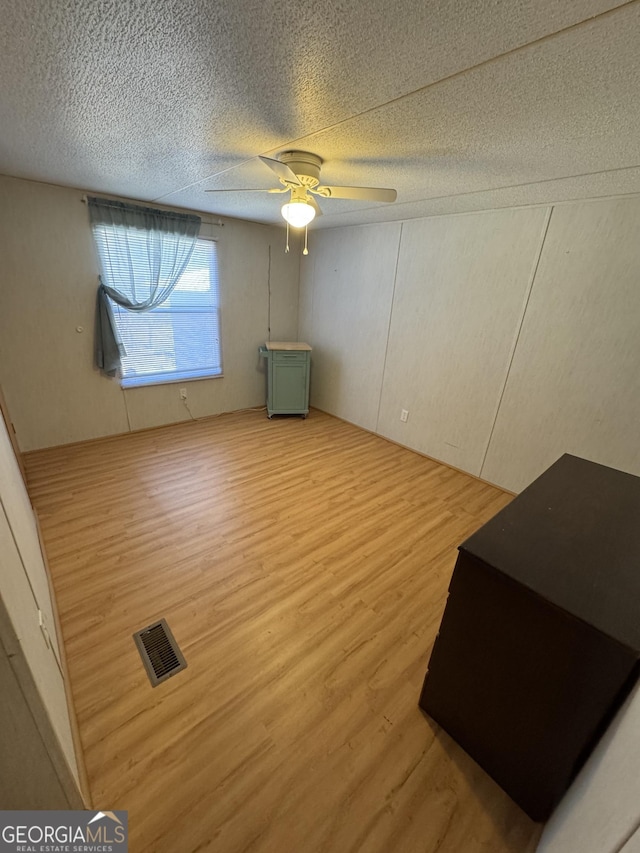 unfurnished bedroom with ceiling fan, wood finished floors, visible vents, and a textured ceiling