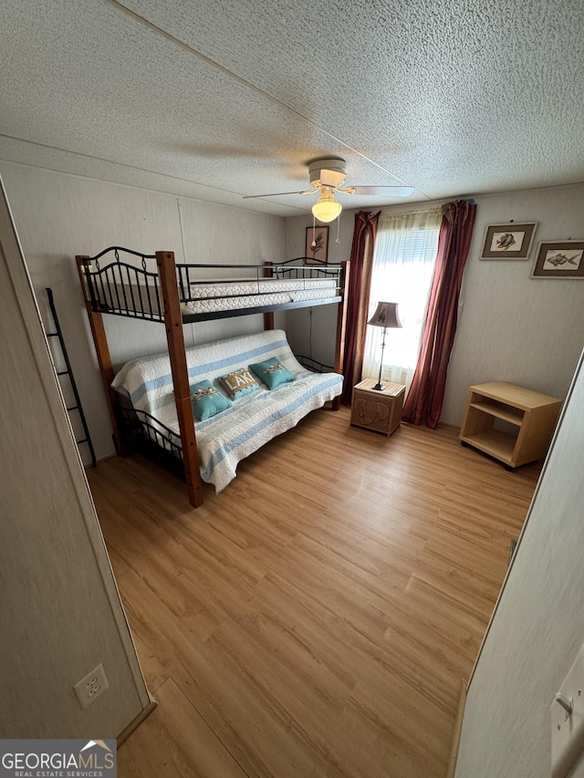 bedroom with a textured wall, a textured ceiling, a ceiling fan, and wood finished floors