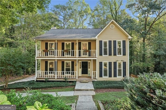 colonial-style house featuring a porch, a balcony, and a chimney