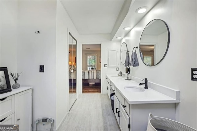 ensuite bathroom featuring double vanity, connected bathroom, wood finished floors, and a sink