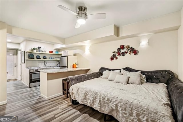 bedroom with baseboards, freestanding refrigerator, wood finished floors, a ceiling fan, and a sink