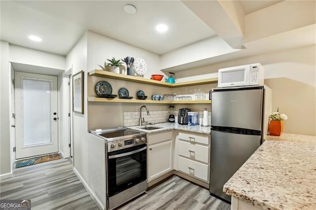 kitchen with light wood finished floors, backsplash, white cabinets, stainless steel appliances, and a sink