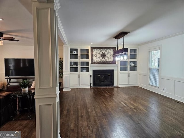 unfurnished living room featuring dark wood-style floors, a ceiling fan, decorative columns, ornamental molding, and a glass covered fireplace