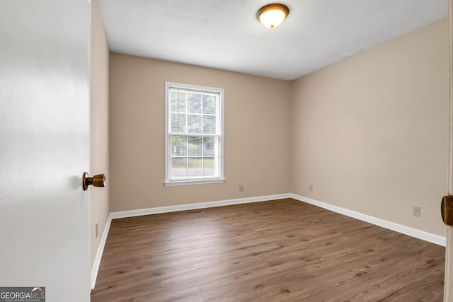 spare room with visible vents, a textured ceiling, baseboards, and wood finished floors