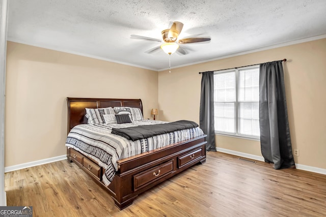 bedroom with ornamental molding, light wood-style floors, baseboards, and a textured ceiling