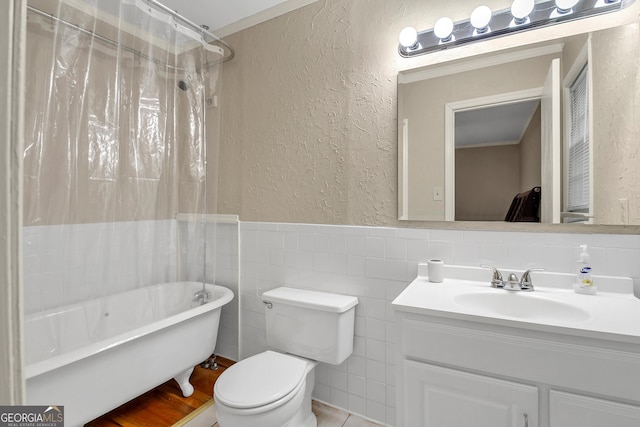 full bathroom featuring toilet, tile walls, crown molding, vanity, and a textured wall