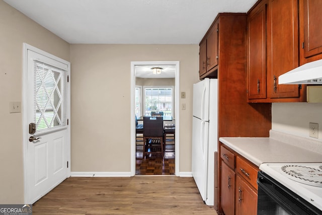 kitchen featuring baseboards, light wood finished floors, freestanding refrigerator, light countertops, and under cabinet range hood