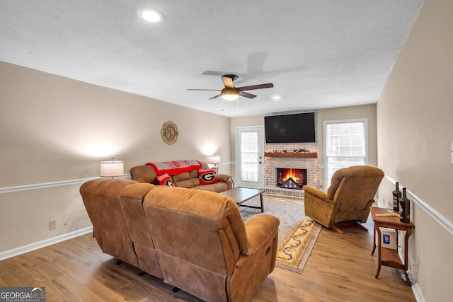 living room featuring a ceiling fan, baseboards, light wood-style flooring, a fireplace, and recessed lighting