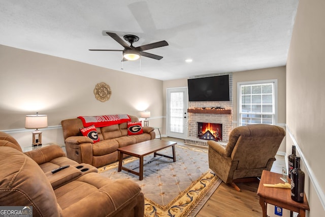 living area with a fireplace, wood finished floors, baseboards, and ceiling fan