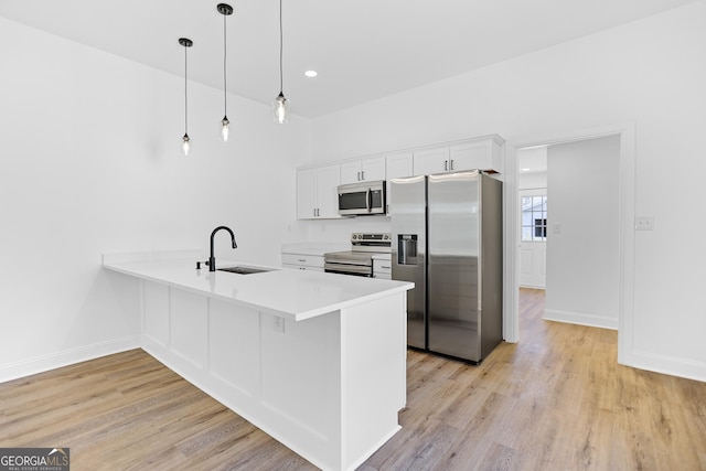 kitchen featuring light countertops, light wood-style flooring, appliances with stainless steel finishes, a peninsula, and a sink