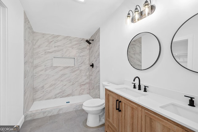 bathroom featuring double vanity, tiled shower, toilet, and a sink