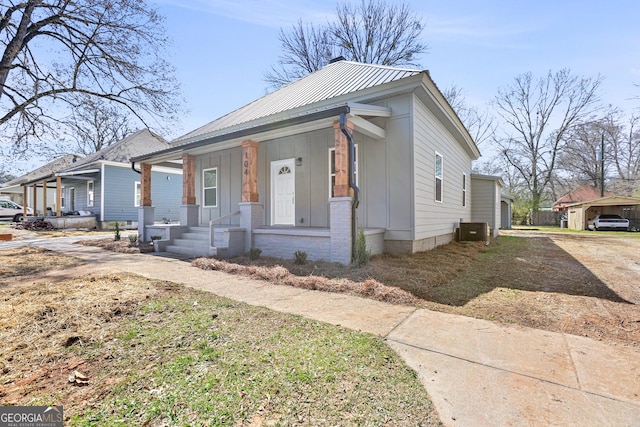 bungalow-style home featuring board and batten siding, a porch, metal roof, a carport, and driveway