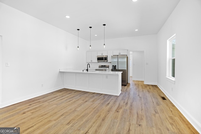 kitchen with a peninsula, stainless steel appliances, light wood-style floors, white cabinetry, and a sink