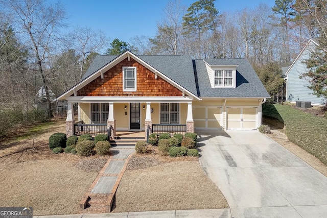 craftsman inspired home featuring central AC unit, covered porch, concrete driveway, and roof with shingles