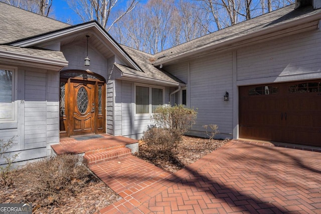 view of exterior entry with a garage and a shingled roof