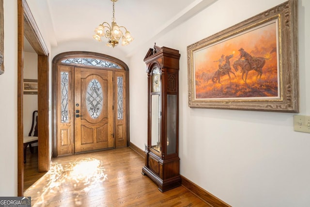 foyer entrance with lofted ceiling, wood finished floors, baseboards, and a chandelier