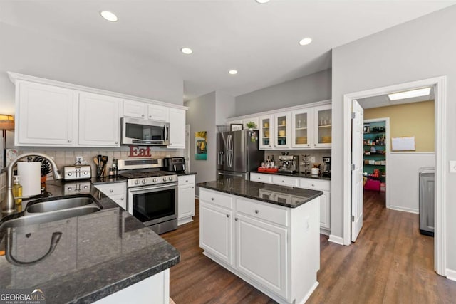 kitchen with a sink, a kitchen island, appliances with stainless steel finishes, decorative backsplash, and dark wood-style flooring