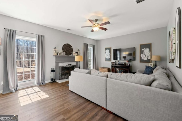 living area with visible vents, a fireplace with raised hearth, baseboards, ceiling fan, and wood finished floors