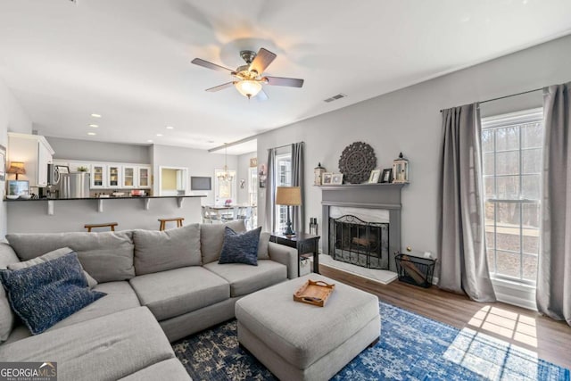 living area with visible vents, a fireplace with raised hearth, a ceiling fan, wood finished floors, and recessed lighting