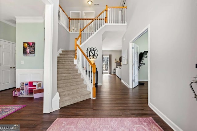 foyer entrance with stairway, wood finished floors, a towering ceiling, and crown molding