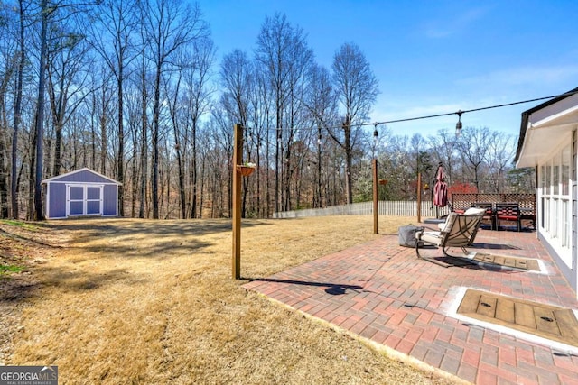 view of yard with a wooded view, fence, a patio area, a storage shed, and an outbuilding