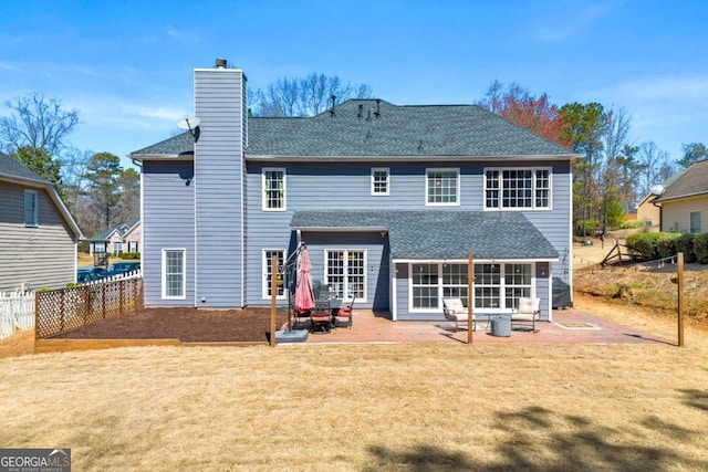 back of house with fence, roof with shingles, a chimney, a patio area, and a lawn