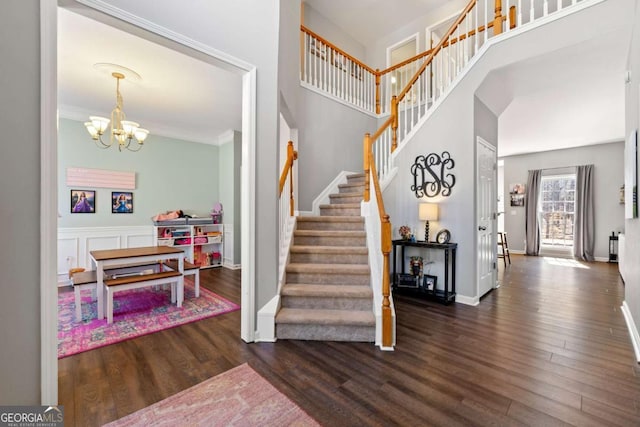 stairway with a notable chandelier, wood finished floors, a towering ceiling, and ornamental molding