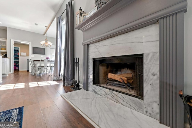 details with a notable chandelier, wood finished floors, visible vents, and a premium fireplace