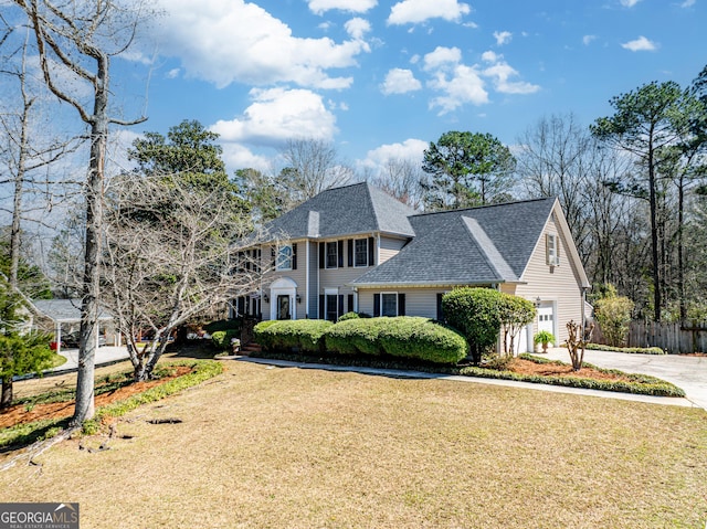 colonial-style house with a garage, roof with shingles, a front lawn, and fence