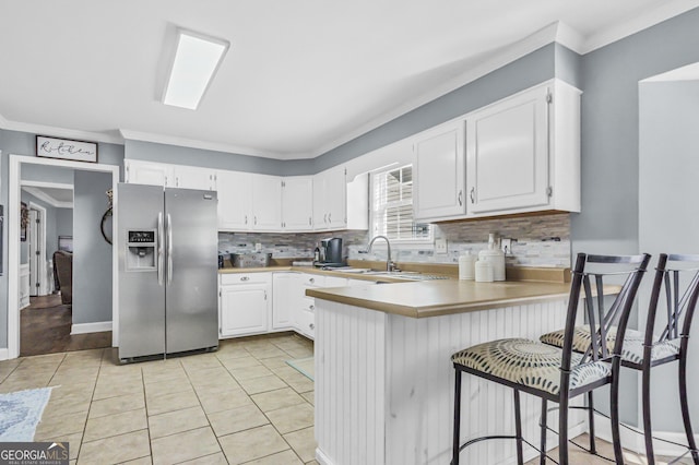 kitchen with stainless steel refrigerator with ice dispenser, a sink, backsplash, white cabinetry, and a peninsula