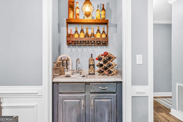 bar featuring wood finished floors, baseboards, wet bar, ornamental molding, and a sink