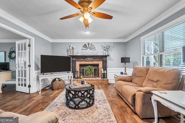 living area with ornamental molding, a fireplace, a ceiling fan, and wood finished floors