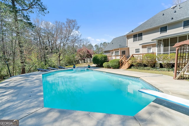 outdoor pool featuring a patio, a wooden deck, a diving board, a sunroom, and stairs